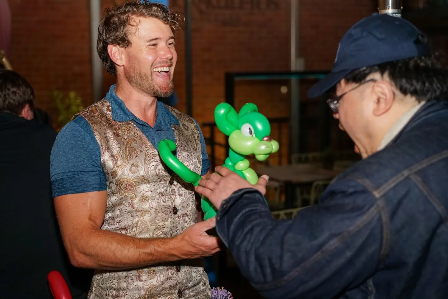 Balloon artist handing a green sculpture to a guest