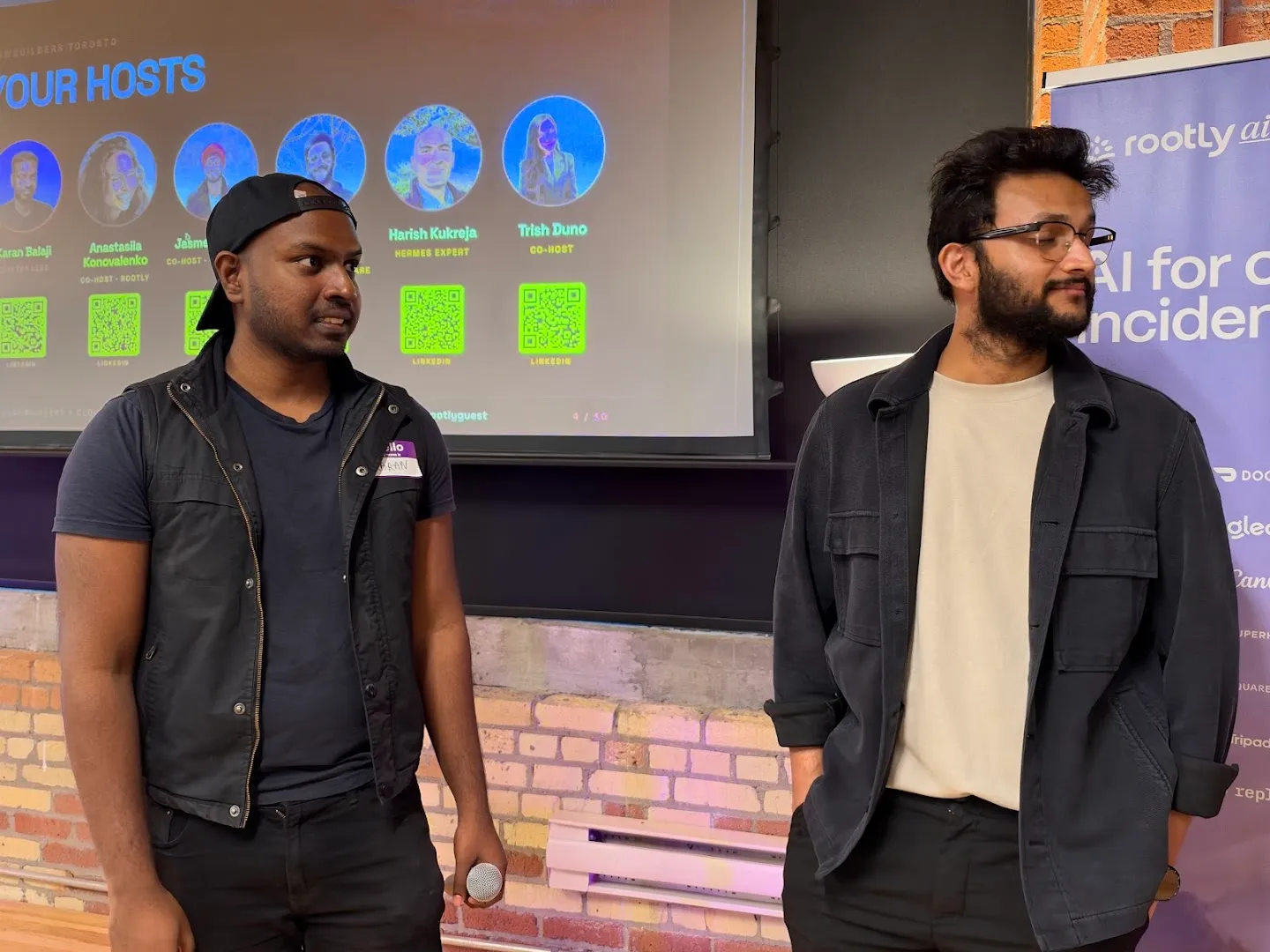 Presenters with microphones beside the screen at the Cloudflare AI agents workshop