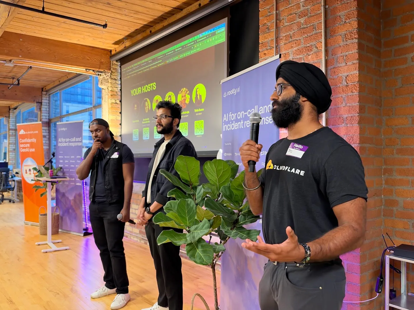 Presenters with microphones beside the screen at the Cloudflare AI agents workshop