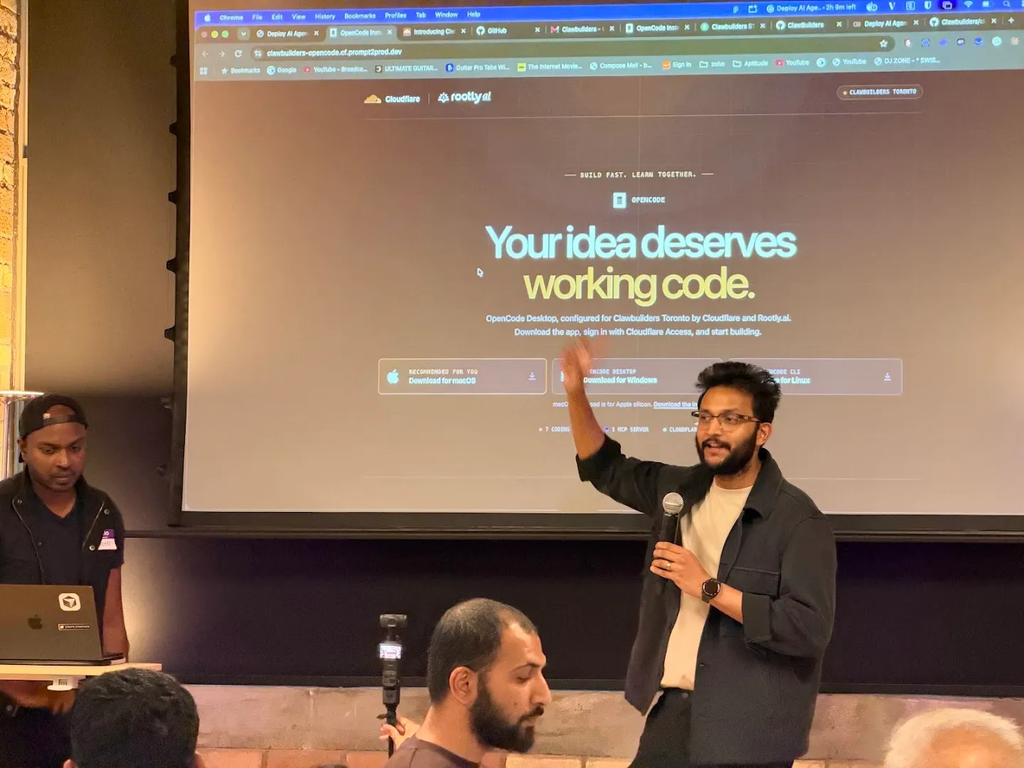 Presenters with microphones beside the screen at the Cloudflare AI agents workshop