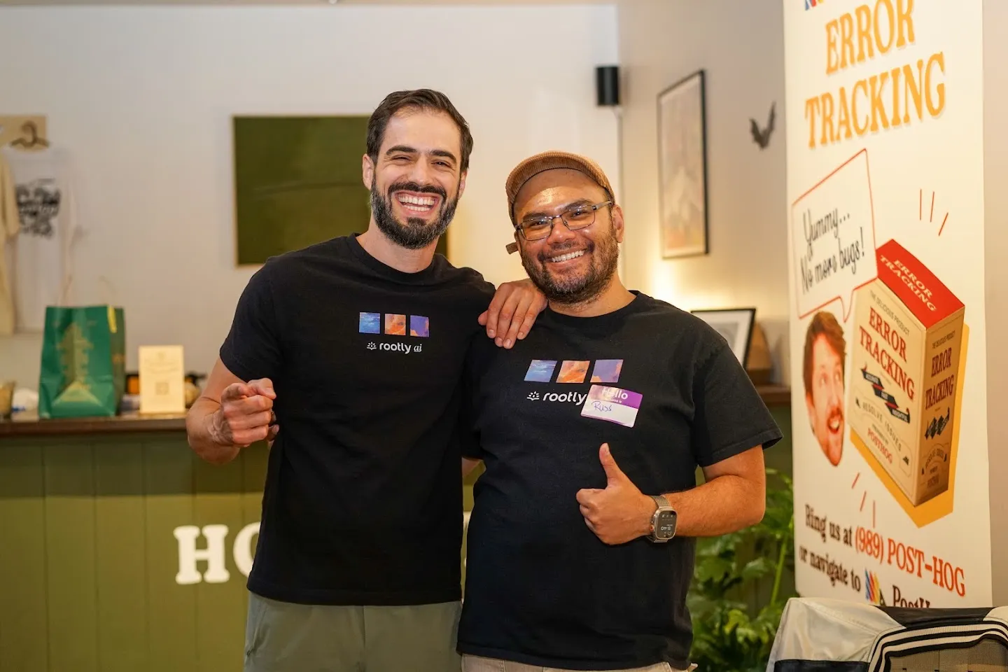 Two Rootly team members posing beside PostHog posters